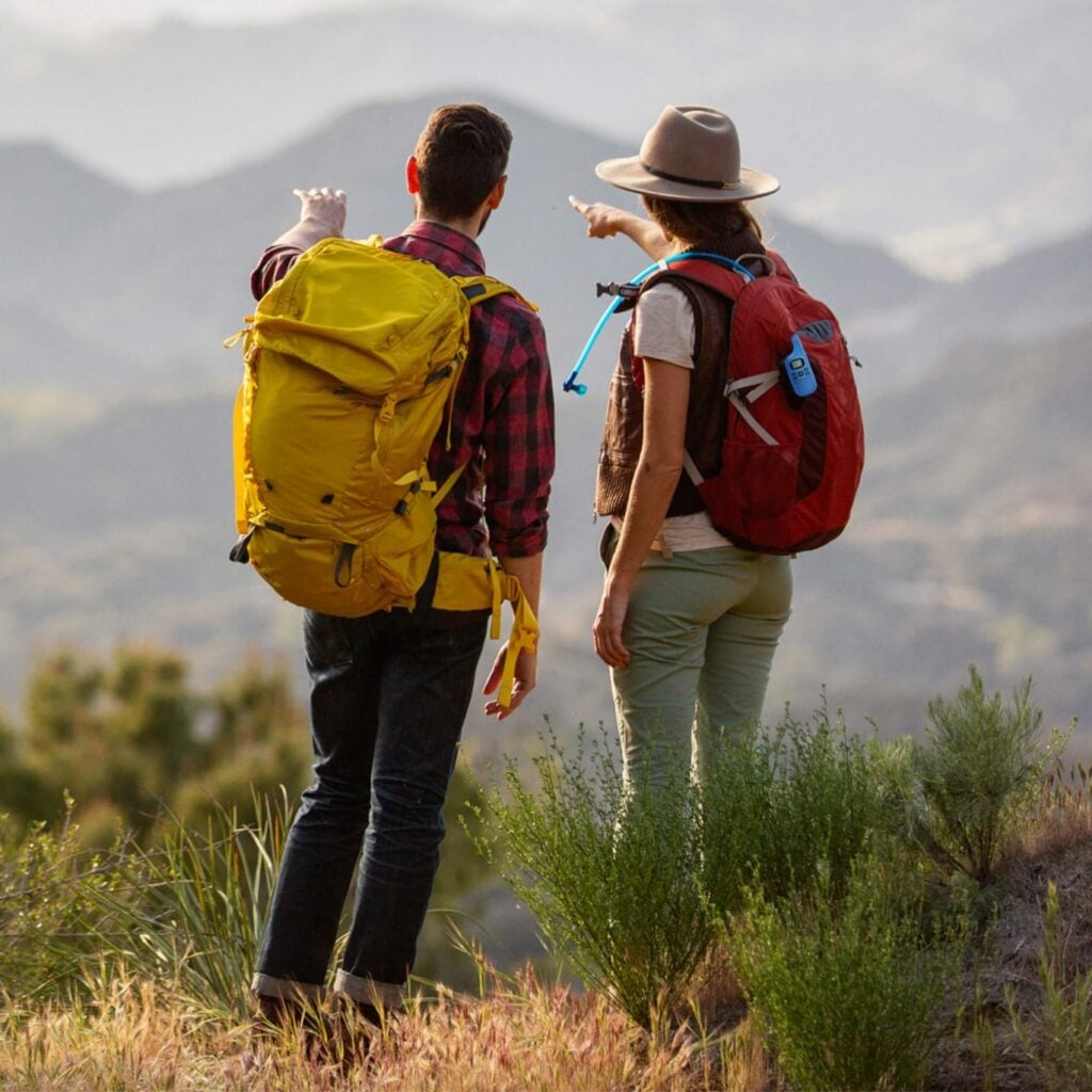 Two people wearing backpacks and pointing towards a mountain