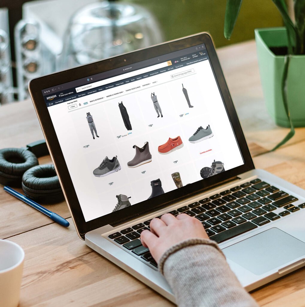 Person shopping on a laptop for fishing apparel and waterproof shoes. Frogg Toggs products displayed on the laptop screen.