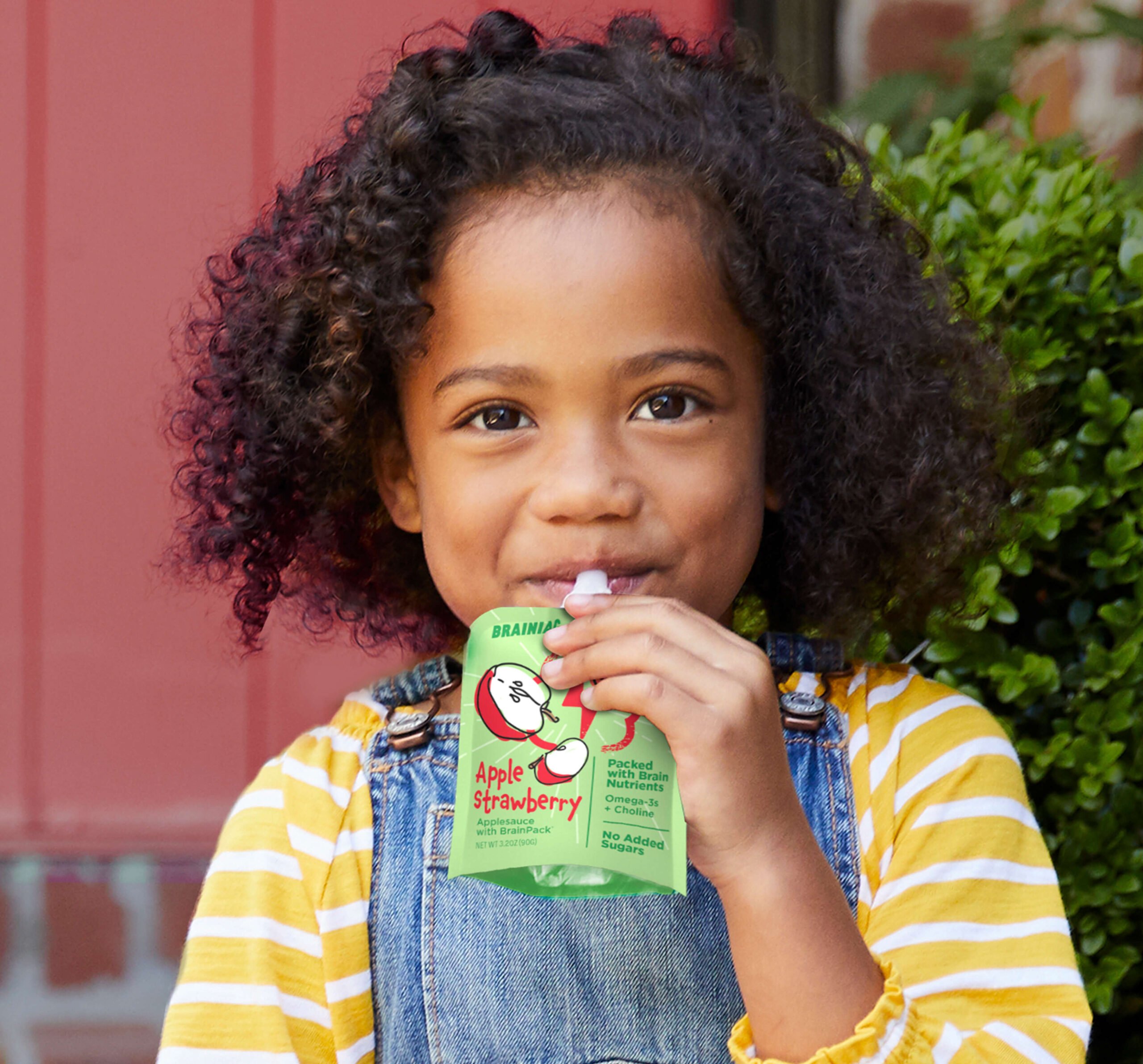 Toddler smiling while eating from a Brainiac Foods pouch